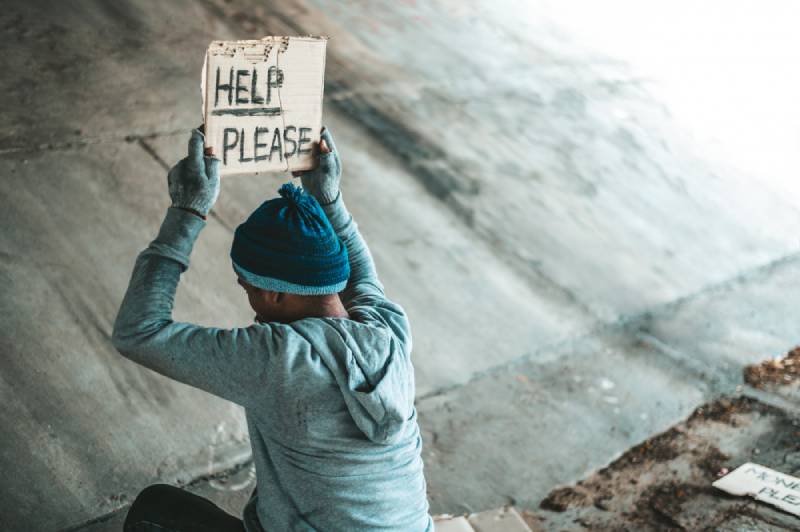Person holding a 'Help Please' sign under a bridge